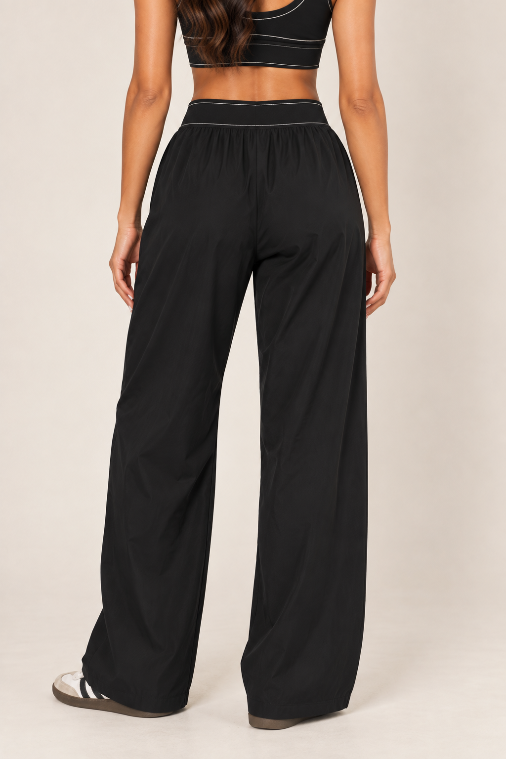 Rear close-up of Glowie black nylon pants showing pale waistband stitching, gathered fabric and wide legs with plain back panels.
