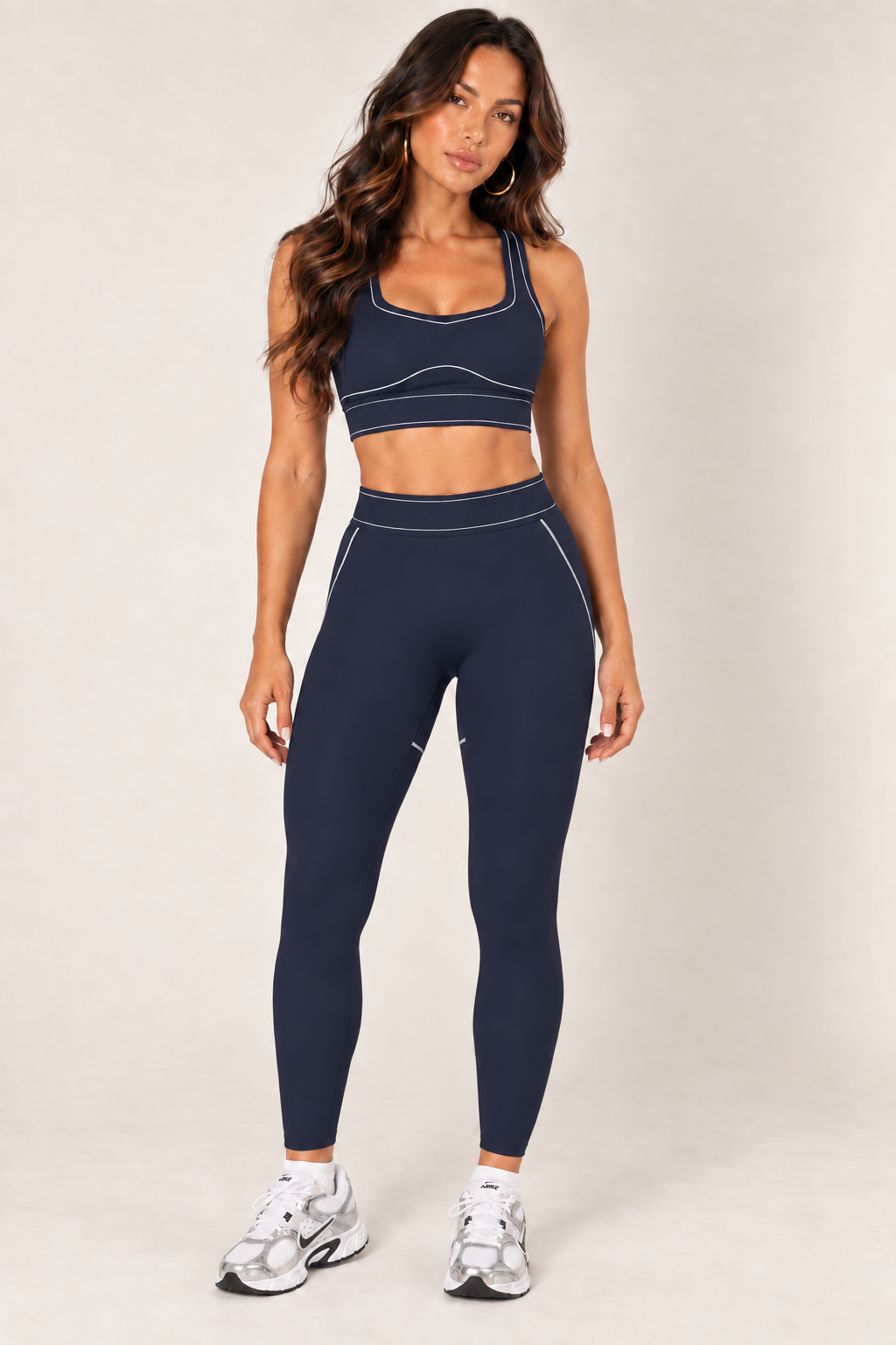 Front view of dark navy high-rise contour leggings with a wide contrast-stitched waistband, styled with a matching sports bra and white, silver and black Nike sneakers.