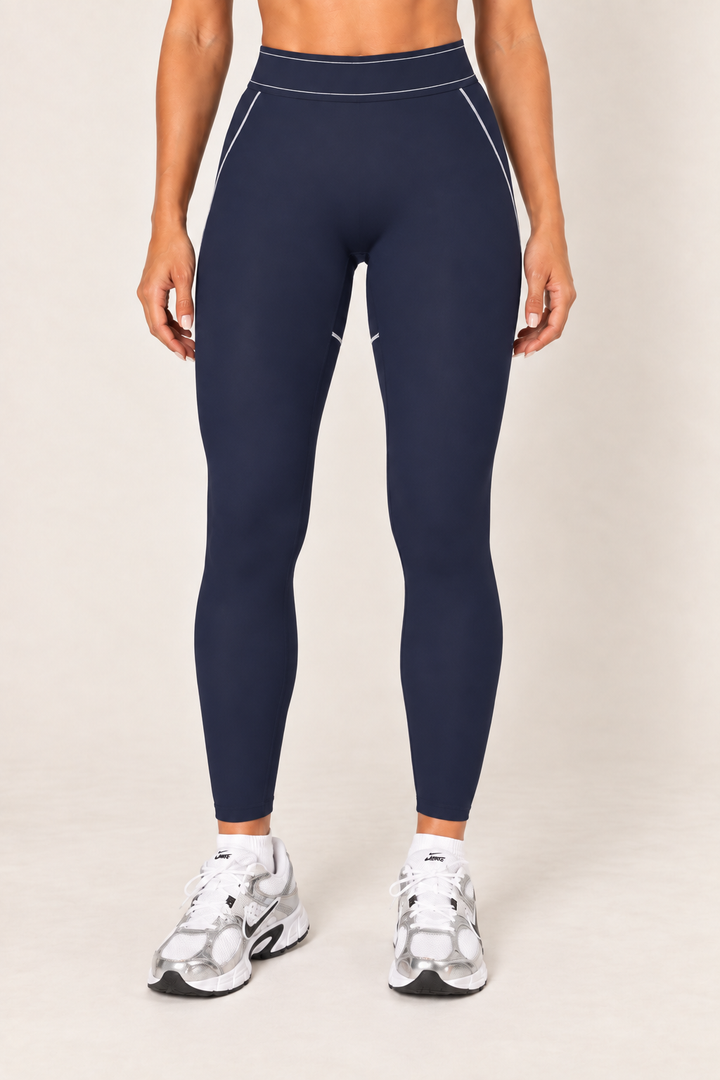 Waist-down front view of dark navy fitted leggings showing the wide high-rise waistband, light contrast seams at the hips and smooth ankle-length legs.