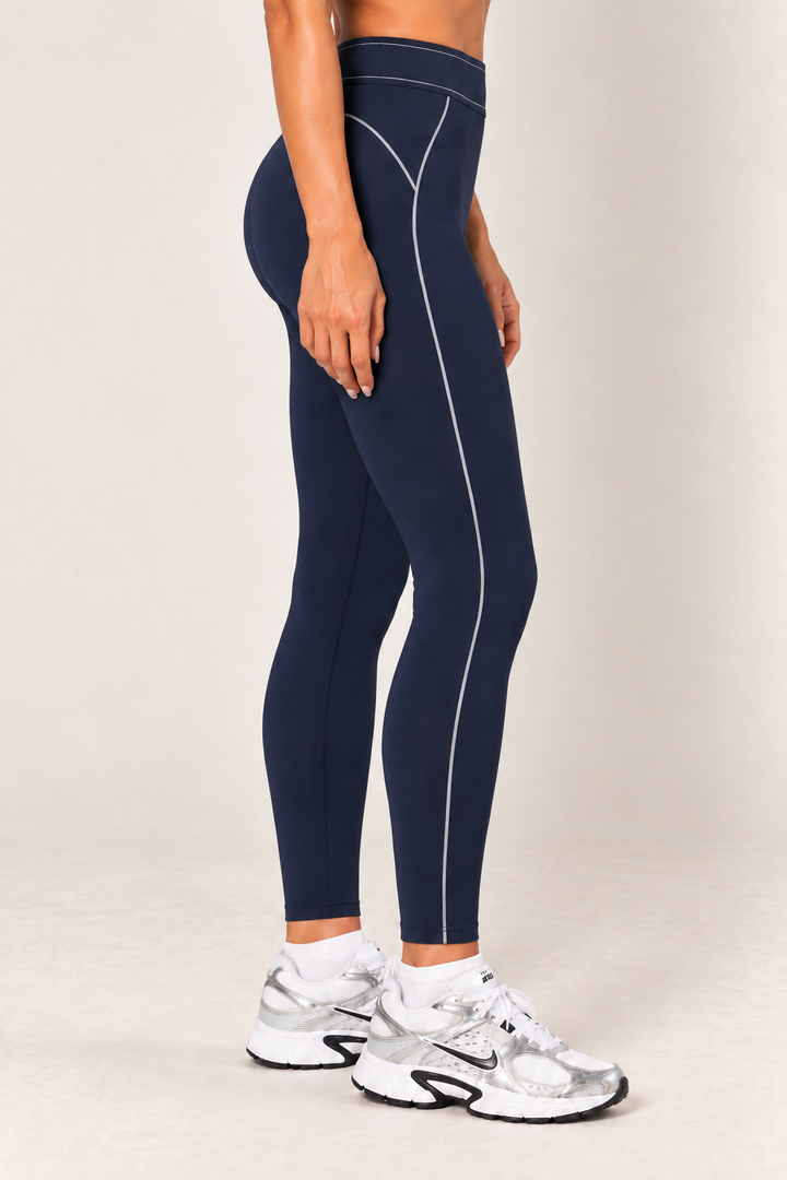 Waist-down side view of dark navy contour leggings highlighting the curved hip seam and light stitching extending down to the ankle-length hem.