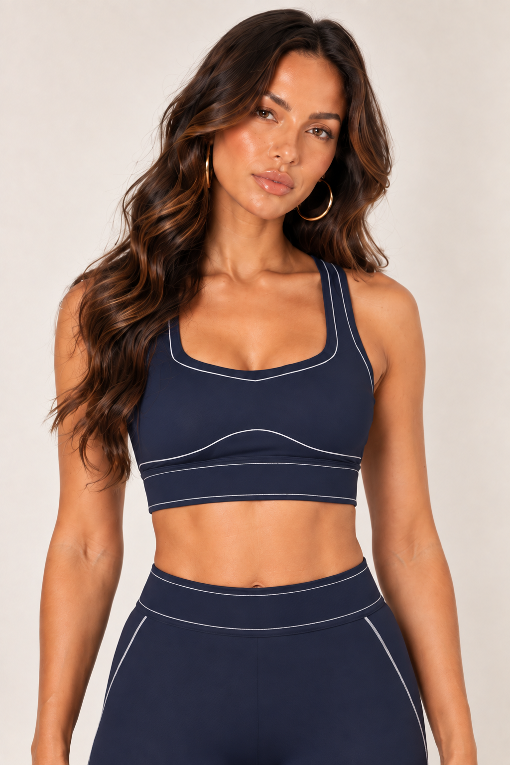 Front close-up of a dark navy sports bra showing wide straps, a shaped neckline, curved front seam and pale contrast stitching across the underband.