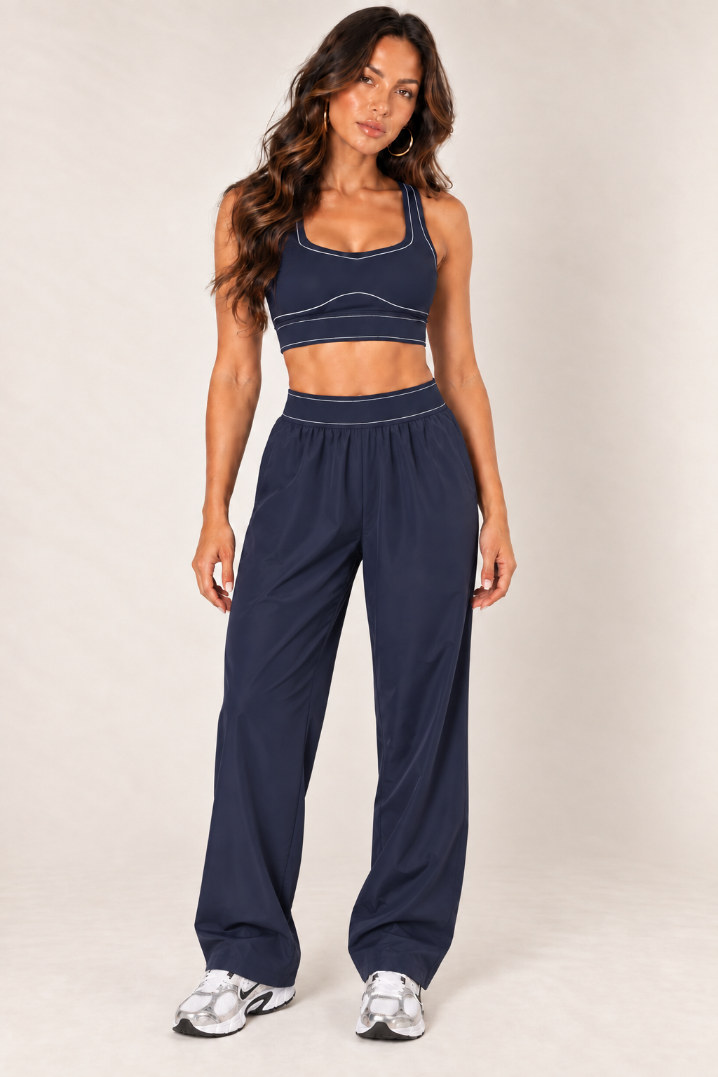 Front view of dark navy contrast thread sports bra paired with matching relaxed nylon track pants and Nike sneakers.