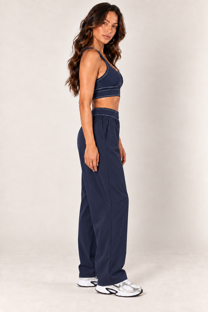 Side view of dark navy contrast thread sports bra paired with matching relaxed nylon track pants and Nike sneakers.