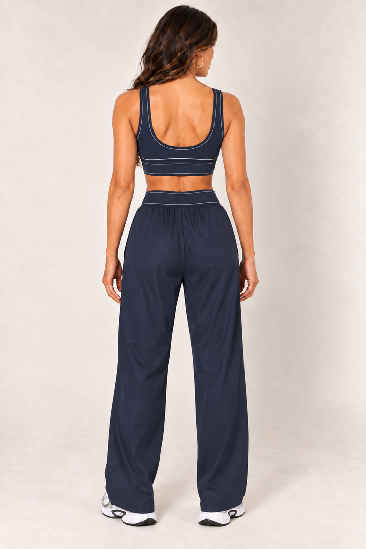 Back view of dark navy contrast thread sports bra paired with matching relaxed nylon track pants and Nike sneakers.