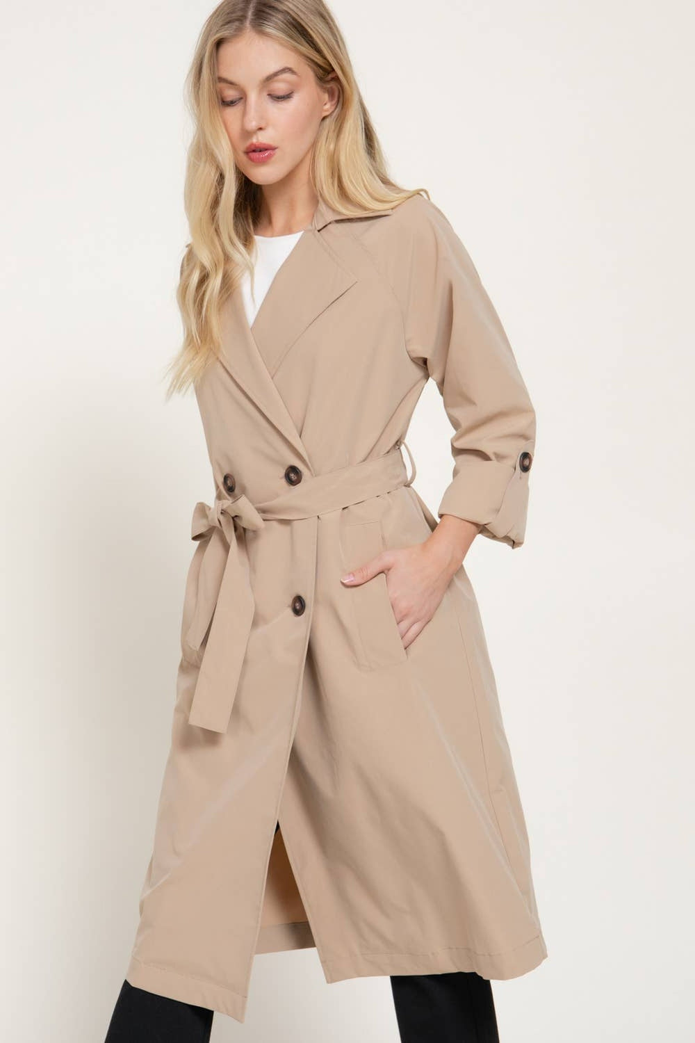Front view of the light khaki double-breasted trench coat belted at the waist with roll-tab sleeves