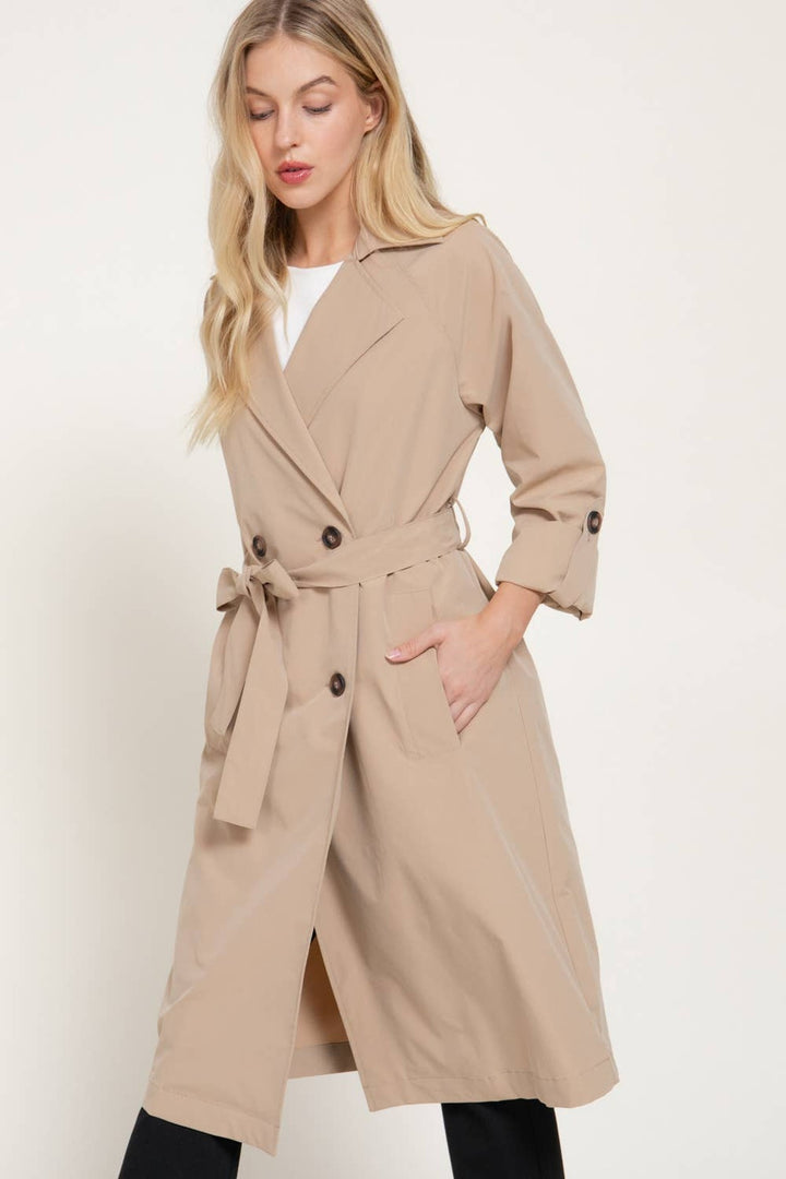 Front view of the light khaki double-breasted trench coat belted at the waist with roll-tab sleeves
