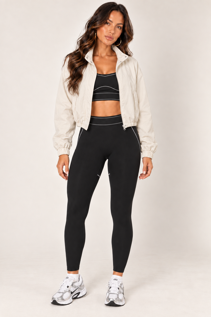 Cream LOVE TREE cropped windbreaker worn open with a black sports bra and leggings; full front outfit view.