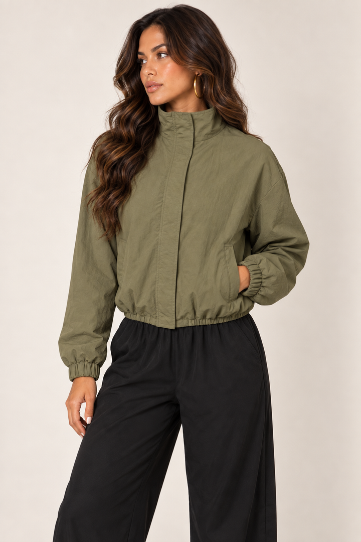 Olive cropped windbreaker with black track pants — thigh up left zipped