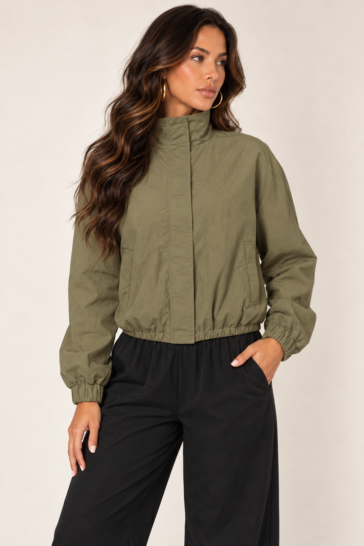 Olive cropped windbreaker with black track pants — thigh up right zipped