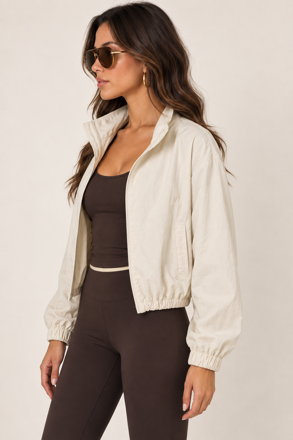 Cream LOVE TREE windbreaker with a chocolate brown athletic tank and leggings, tortoiseshell aviators; thigh-up left, open.