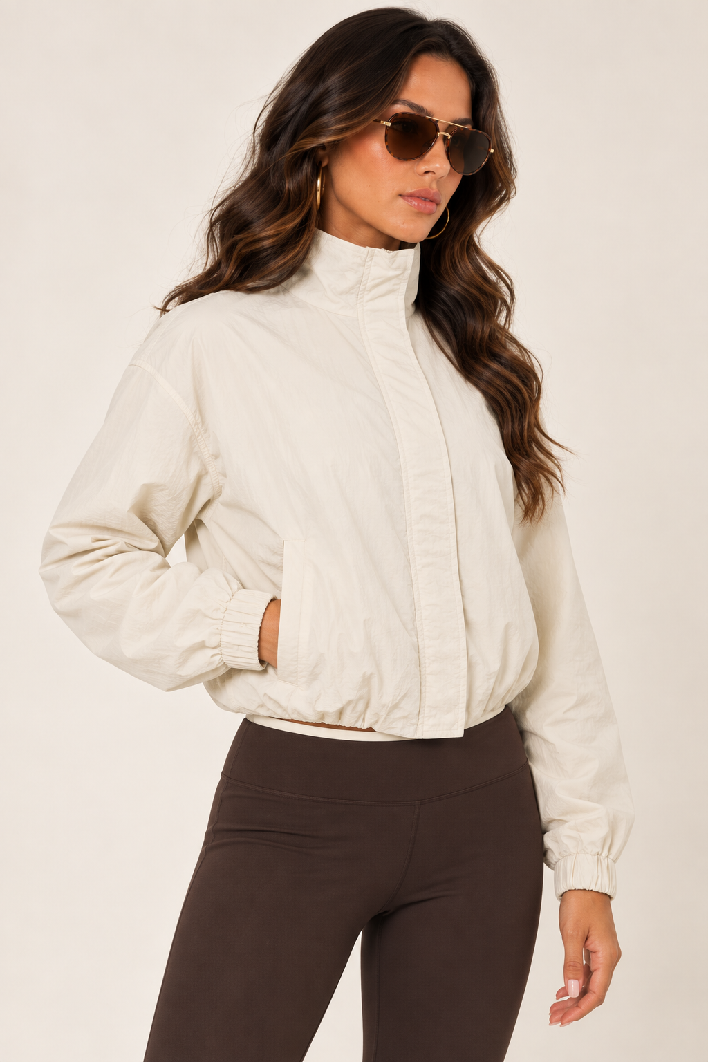 Cream LOVE TREE windbreaker with a chocolate brown athletic tank and leggings, tortoiseshell aviators; thigh-up right, fully zipped.