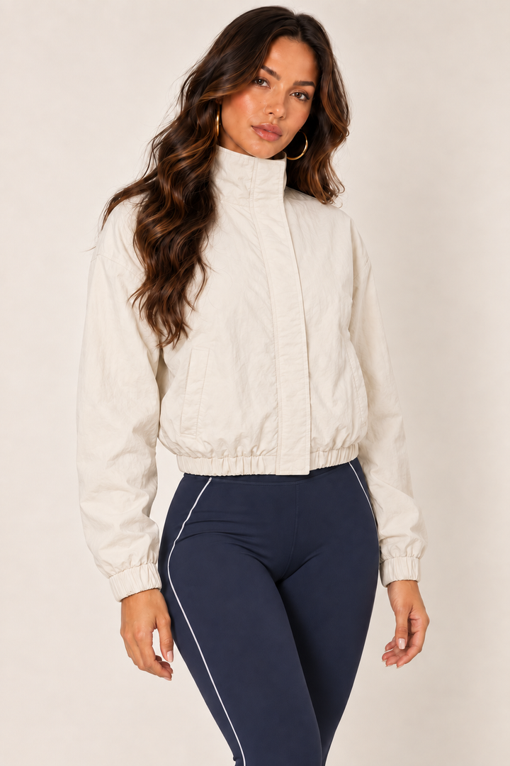 Cream LOVE TREE cropped windbreaker with dark navy sports bra and leggings; thigh-up, fully zipped.