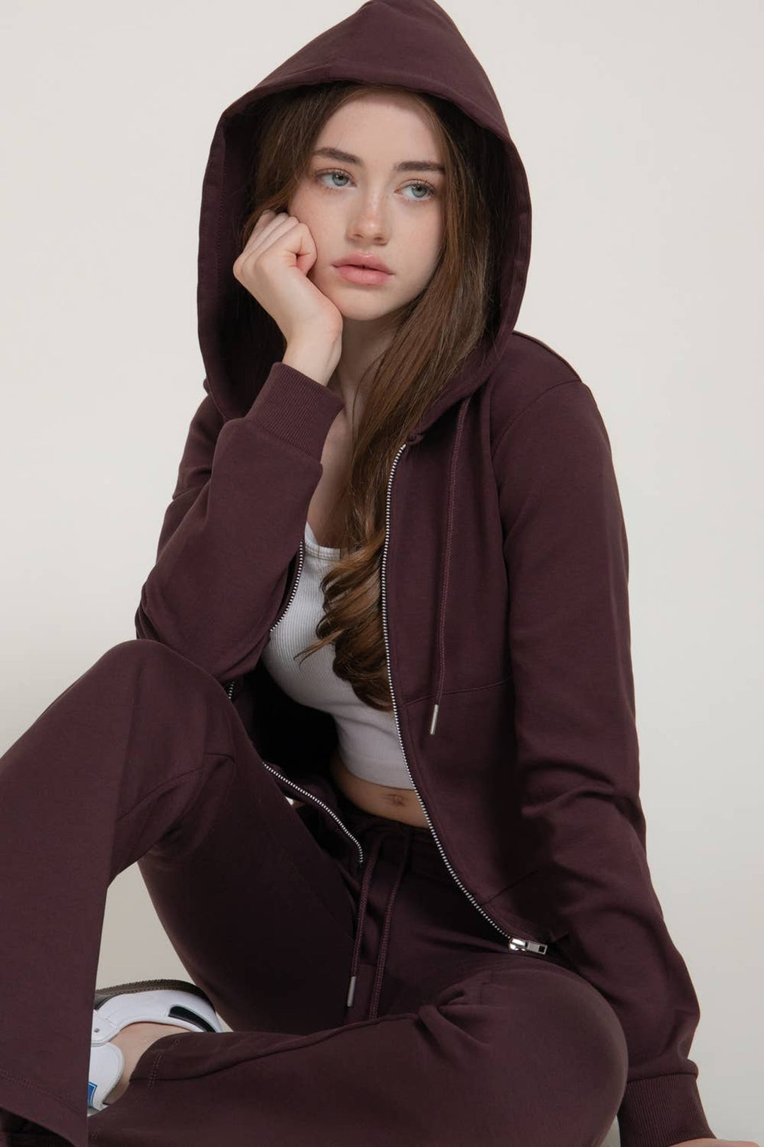 Seated view of the maroon hoodie knit jacket with the hood up over a white tank