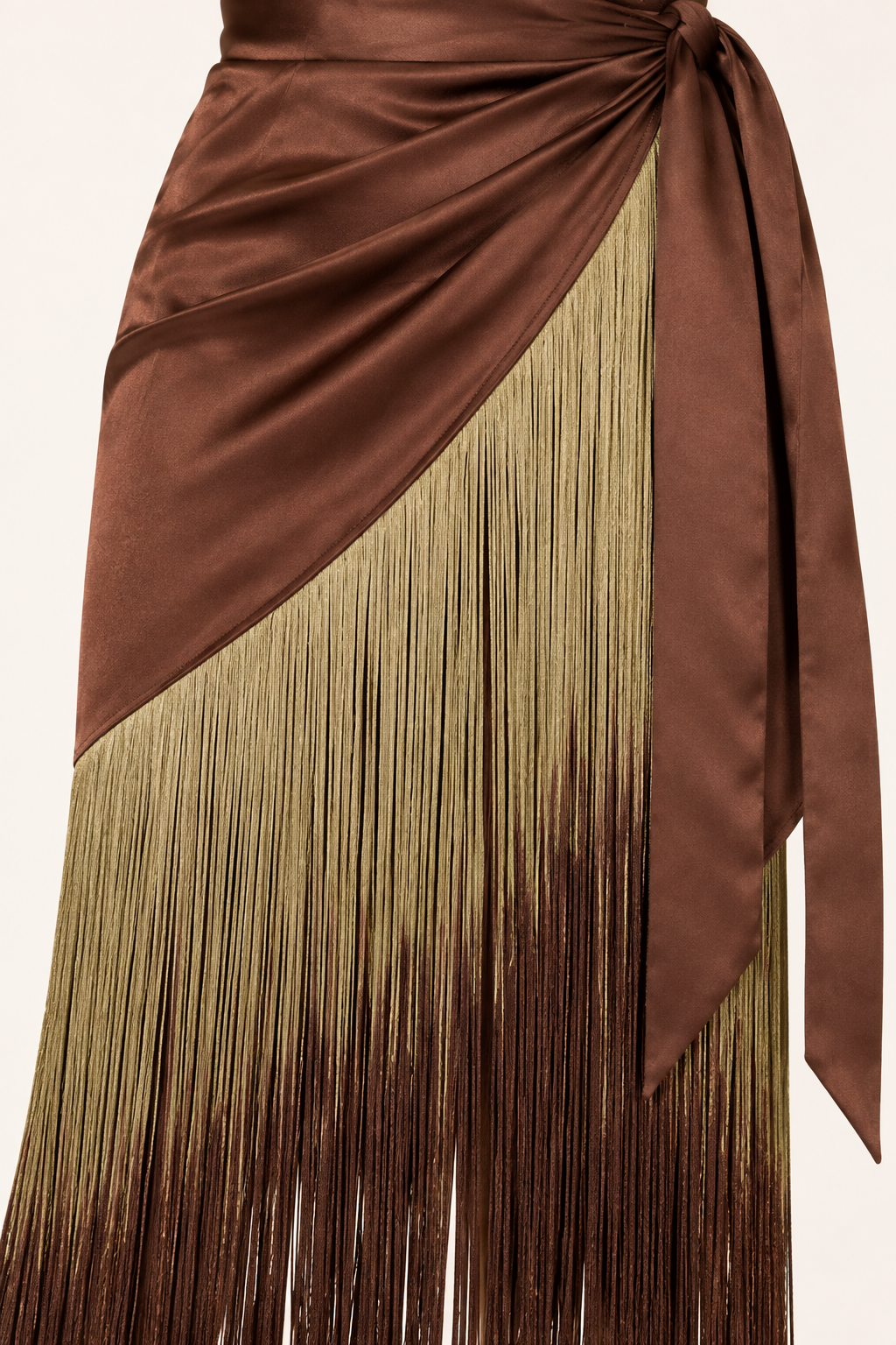 Product-only close-up of the Brown Ombre Fringe Halter Dress by Skylar Rose at Styled by ALX. Fine strands of antique-gold fringe fade into brown beneath the diagonal chocolate-brown satin skirt edge, with the matching satin waist tie alongside. The image shows the dense thread texture and attachment seam on an ivory background.