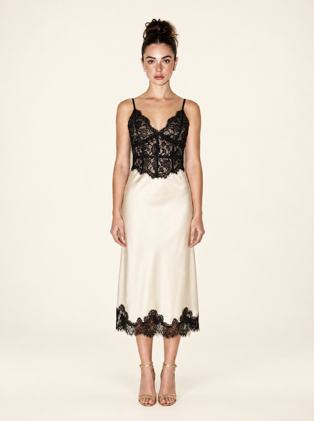 Full-length front view of the Ivory Black Lace Midi Dress by Skylar Rose at Styled by ALX. The model wears a fitted black floral lace bodice with thin straps and a scalloped neckline, an ivory satin midi skirt with black lace hem, and gold strappy open-toe heels against an ivory studio backdrop.