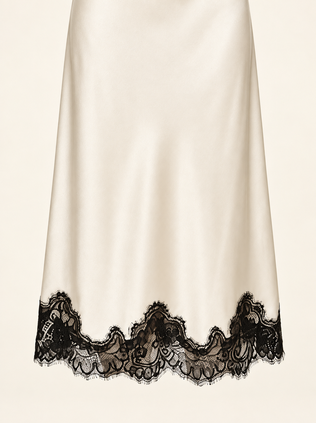 Product-only hem detail of the Ivory Black Lace Midi Dress by Skylar Rose at Styled by ALX. A close view of the ivory satin skirt shows its smooth sheen and the wide, irregular scalloped border of black floral lace, with delicate eyelash edges visible against a pale background.