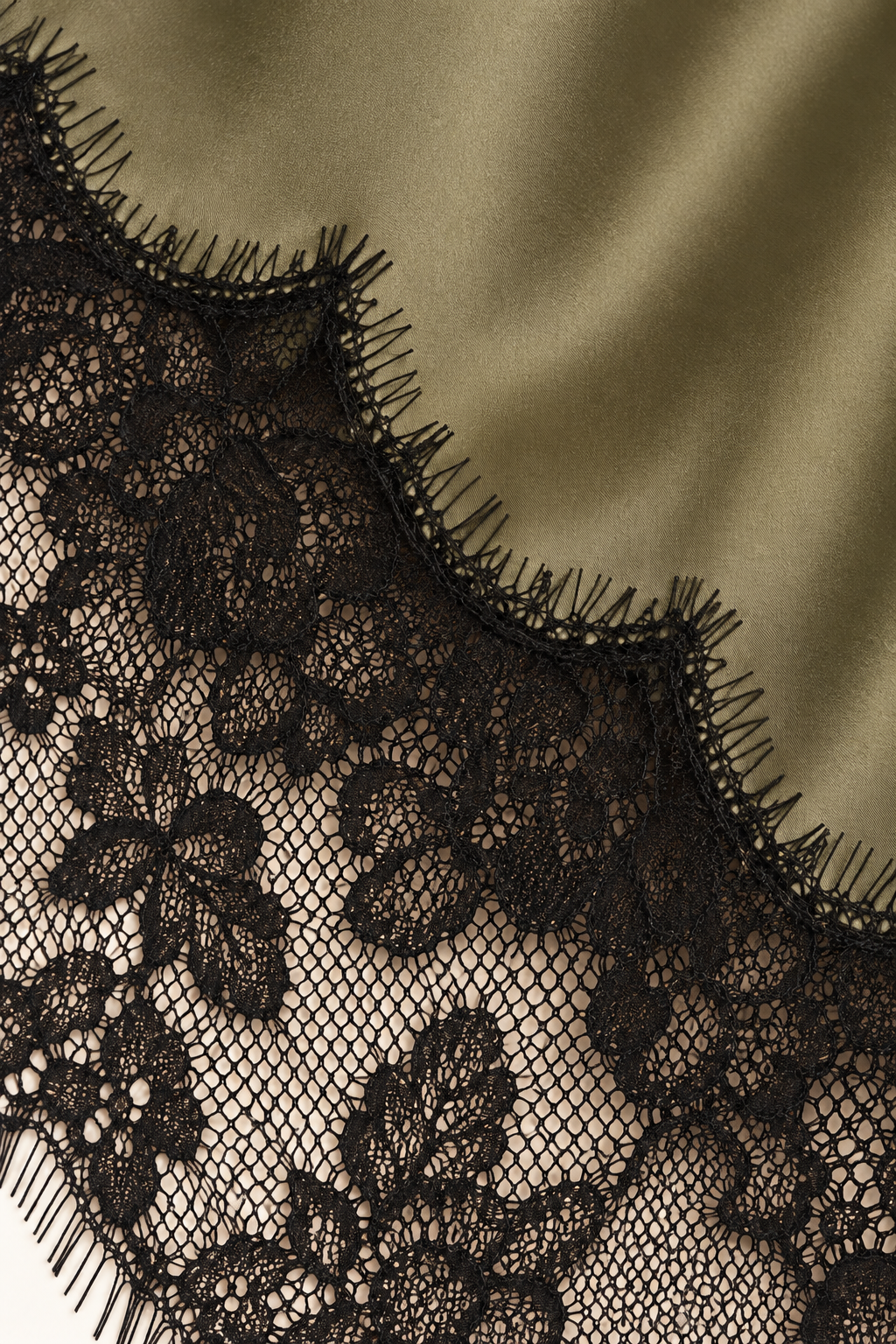Product-only cami hem detail from the Khaki Satin Lace Pants Set by Skylar Rose at Styled by ALX. Olive-khaki satin meets a broad black scalloped floral lace border along the elongated asymmetric hem, highlighting the fine eyelash edging and contrast between smooth satin and lace.