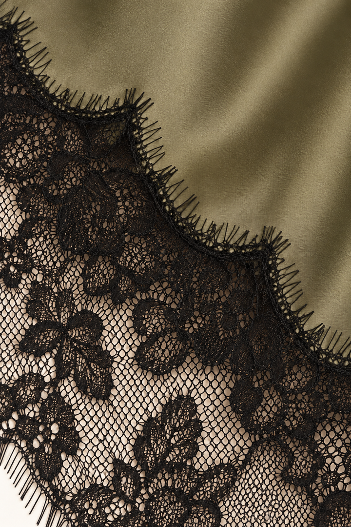 Product-only cami hem detail from the Khaki Satin Lace Pants Set by Skylar Rose at Styled by ALX. Olive-khaki satin meets a broad black scalloped floral lace border along the elongated asymmetric hem, highlighting the fine eyelash edging and contrast between smooth satin and lace.