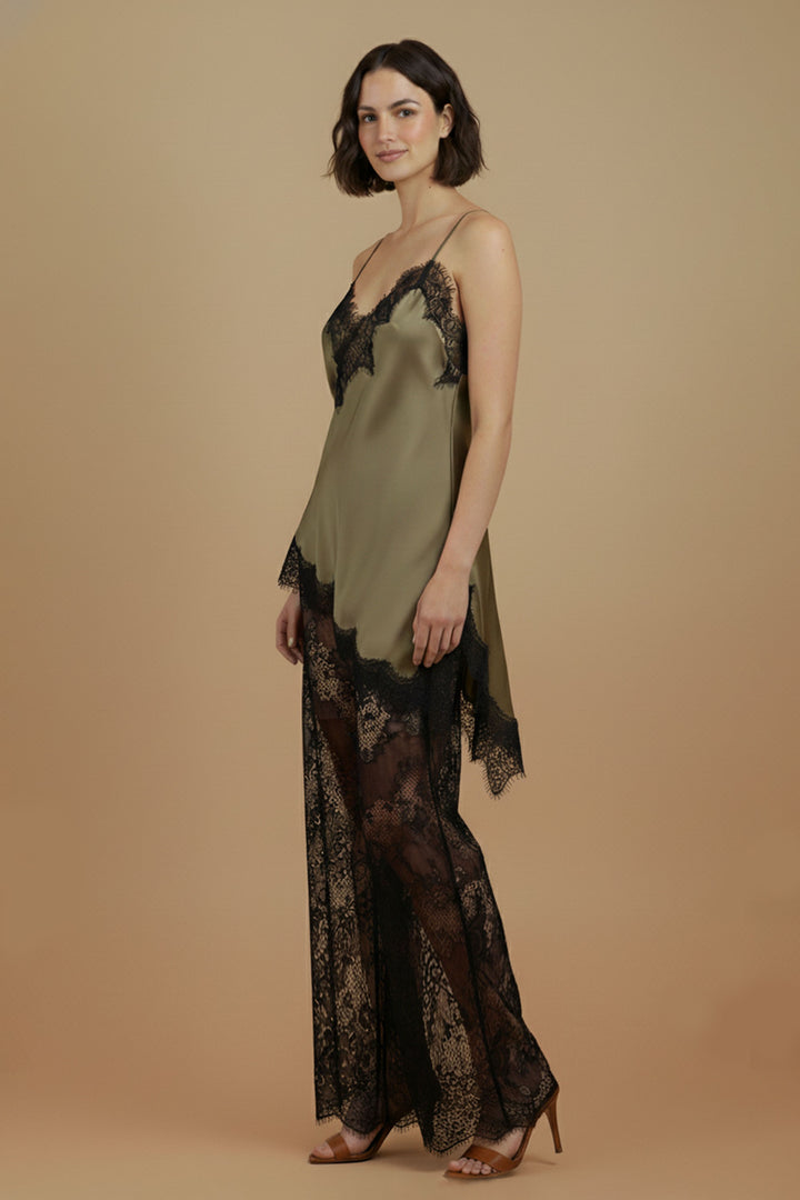 Side and three-quarter model view of the Khaki Satin Lace Pants Set by Skylar Rose at Styled by ALX. The loose olive satin camisole falls into a long asymmetric black lace hem above black floral lace wide-leg trousers, with the model wearing tan open-toe heels.