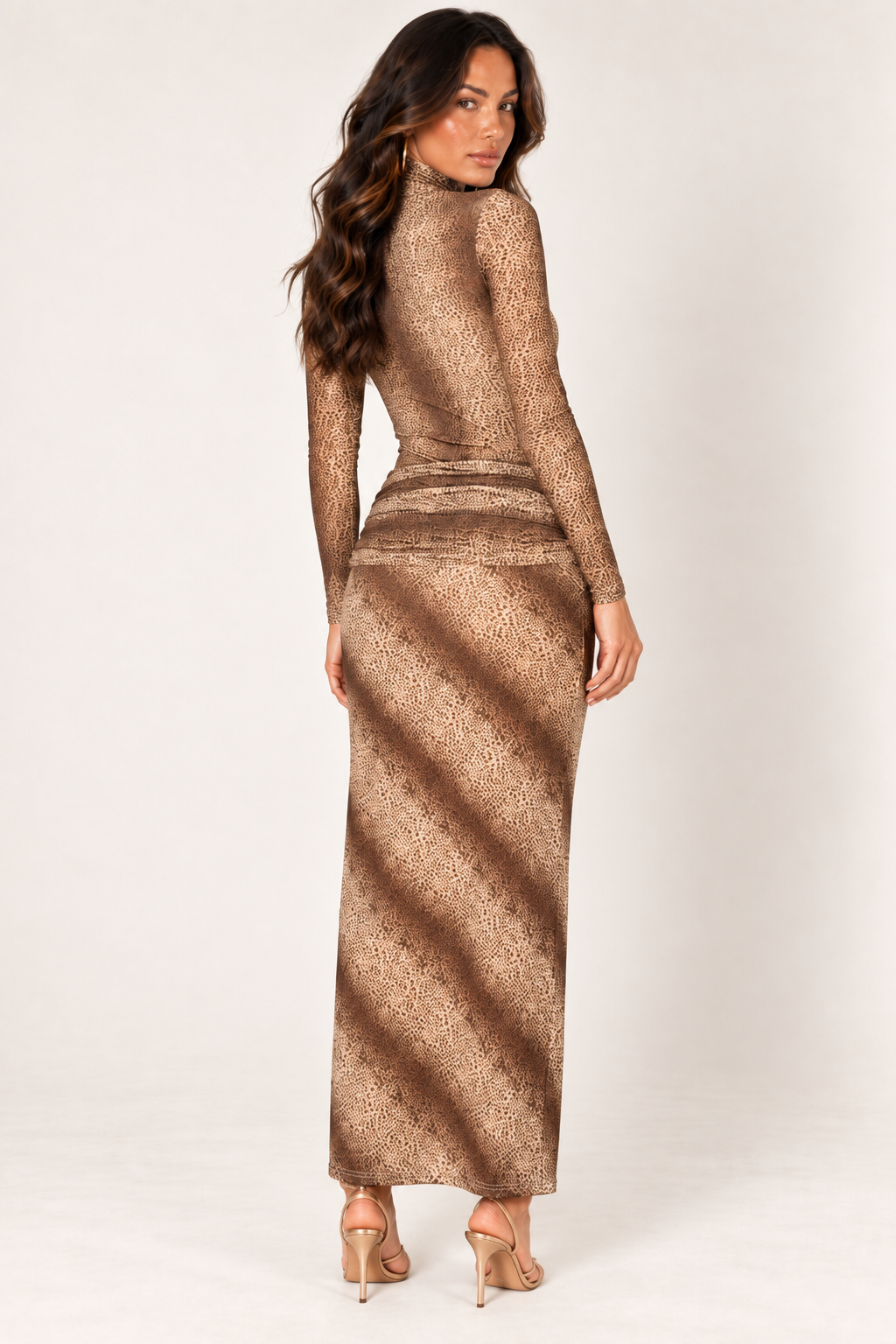 Back view of the Brown Animal Print Skirt Set at Styled by ALX, showing the smooth fitted bodysuit and matching long skirt with gathered fabric across the hips. Fine brown animal markings and diagonal shaded bands cover the warm tan fabric, styled with gold ankle-strap heels.