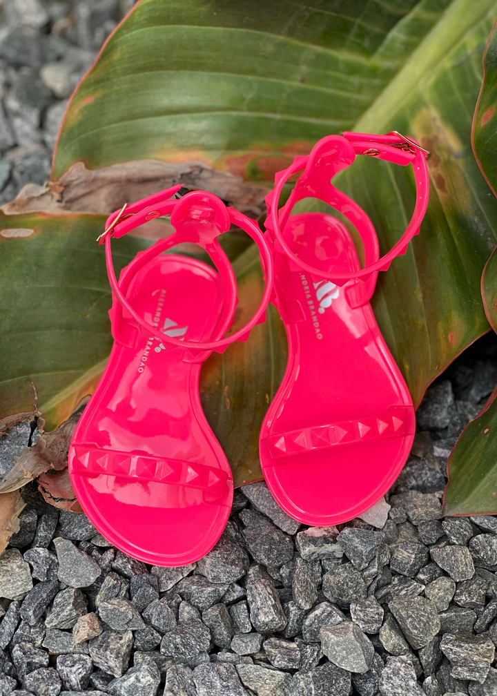 Aria Kids neon pink jelly sandals with thin strap across the toes and thin ankle strap. Shoes for beach and pool days. Wear them all year long with a casual chic look