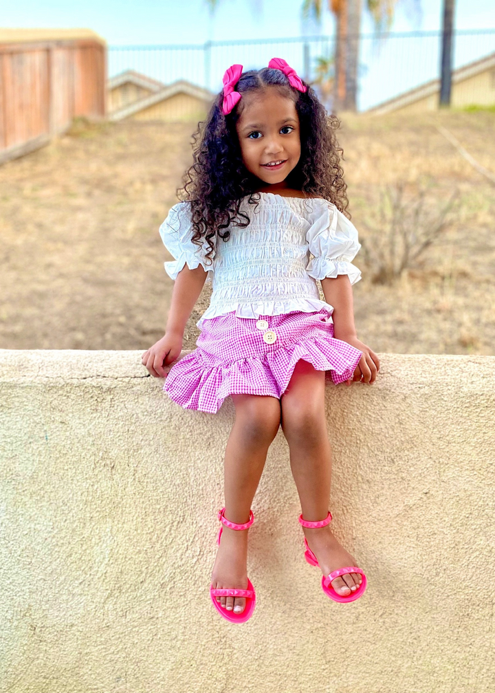 Aria Kids neon pink jelly sandals with thin strap across the toes and thin ankle strap. Shoes for beach and pool days. Wear them all year long with a casual chic look